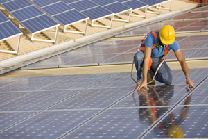 photo of man with yellow hard hat and harness kneeling down on photovoltaic arrays